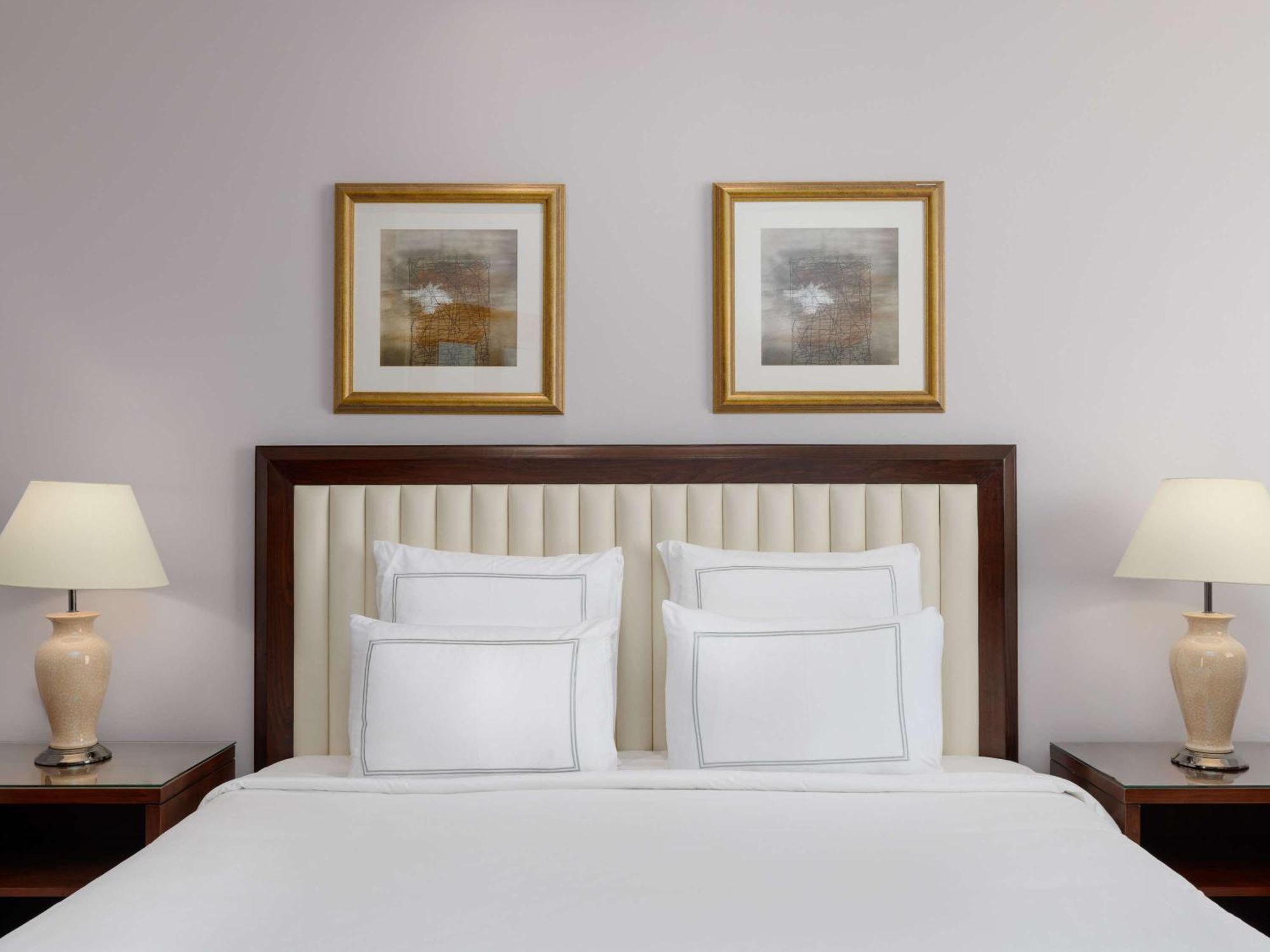 Swissotel Al Maqam Makkah Mekka Eksteriør billede The photo shows a well-decorated bedroom. The focal point is a neatly made bed with white bedding and several white pillows. Behind the bed, there is an upholstered headboard that has a vertical panel design. On either side of the bed, there are beds