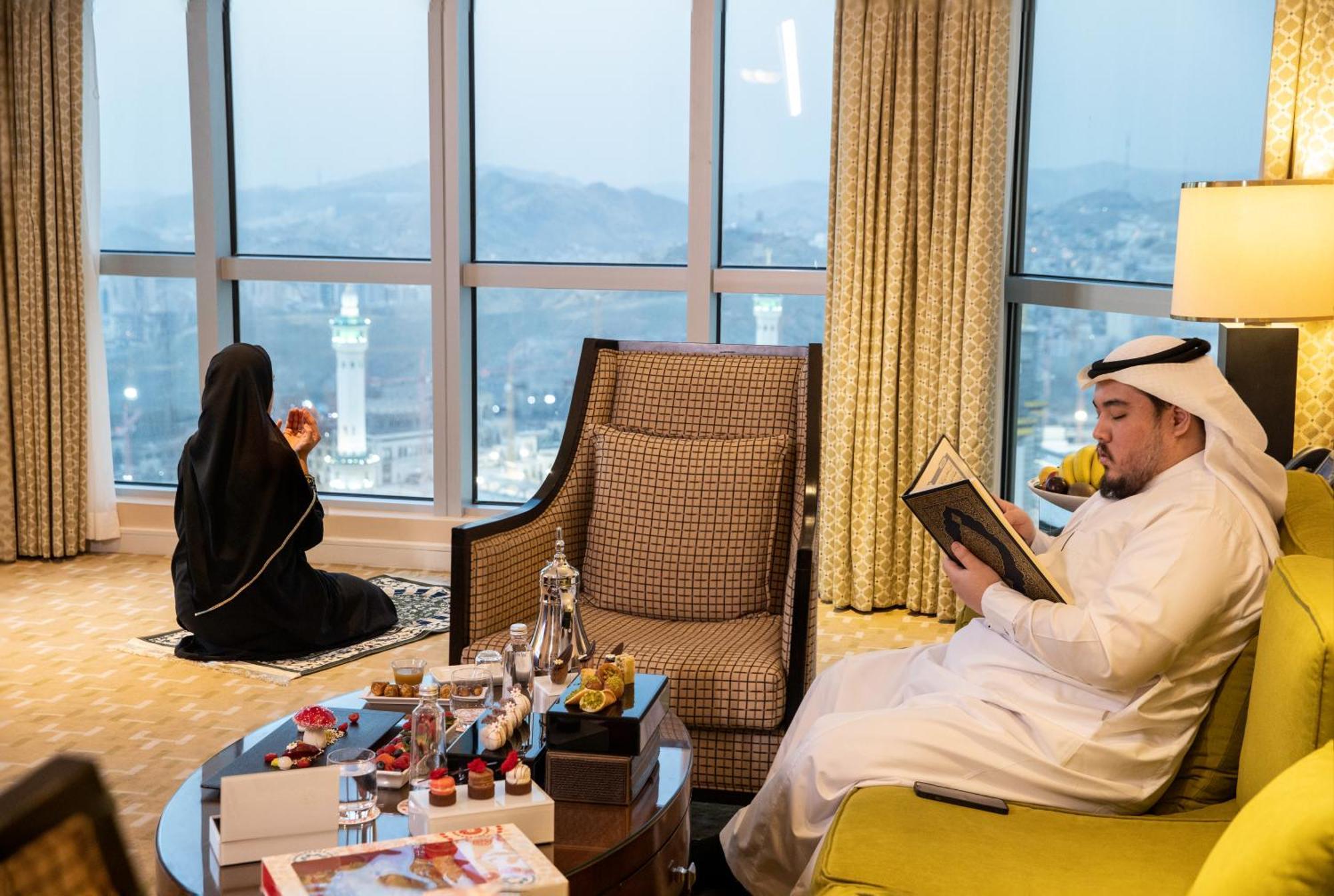Swissotel Al Maqam Makkah Mekka Eksteriør billede The photo depicts a scene inside a hotel room or a suite with large windows providing a view of a cityscape, likely near a landmark. 

In the foreground, there is a stylish coffee table adorned with several decorative items, possibly including small 