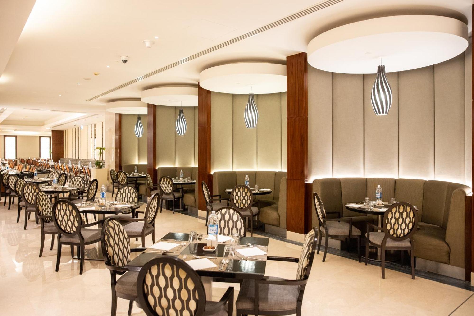 Swissotel Al Maqam Makkah Mekka Eksteriør billede The photo shows a stylish restaurant interior. It features several dining tables arranged neatly with elegant chairs that have a patterned design. The walls are adorned with soft, muted colors and have wooden accents. Ambient lighting is provided by 