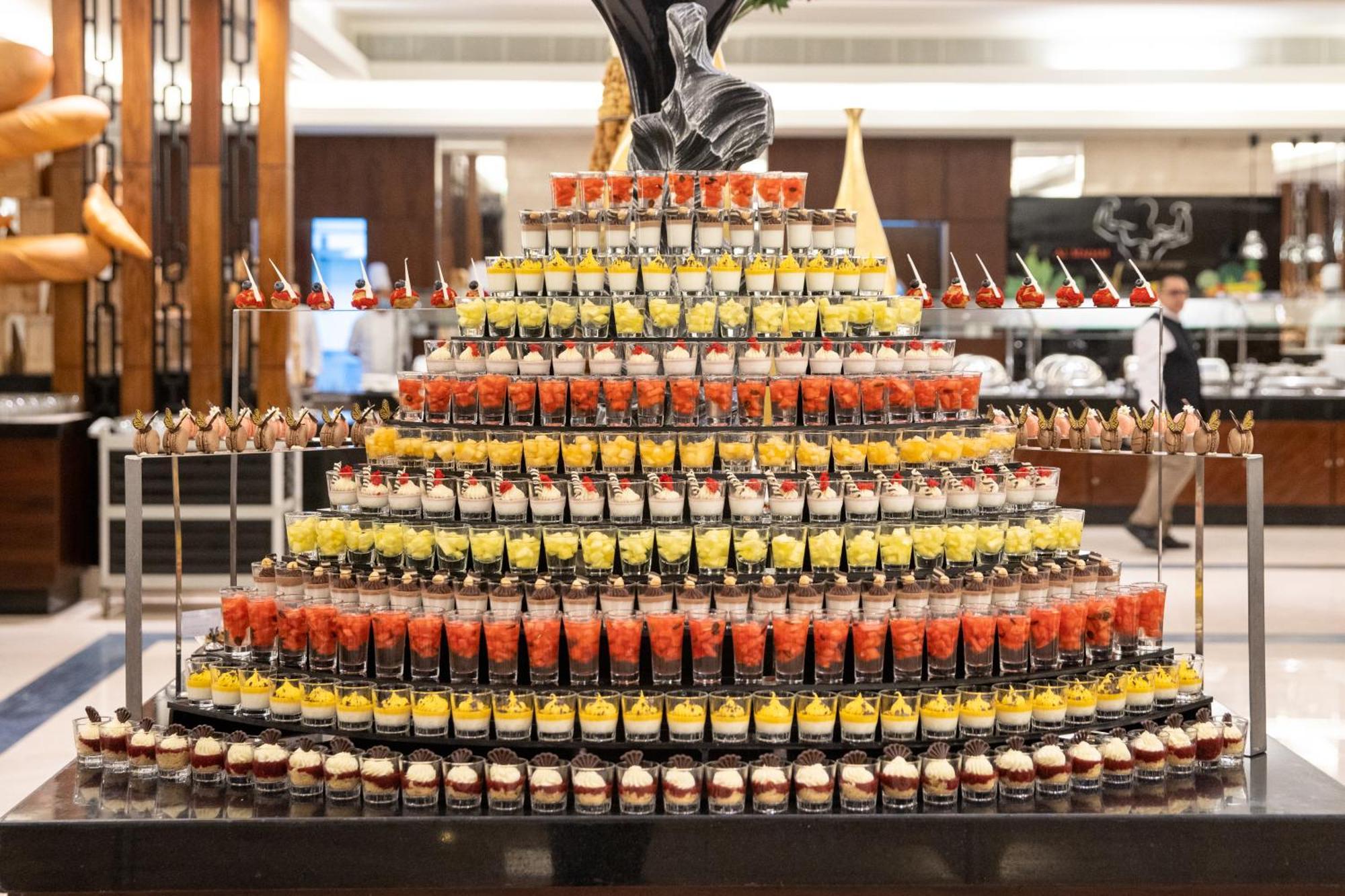 Swissotel Al Maqam Makkah Mekka Eksteriør billede The photo shows an elaborate display of desserts arranged in a tiered, pyramid-like structure. The arrangement consists of numerous small cups filled with various colorful desserts, including layers of fruity and creamy elements. The cups are stacked