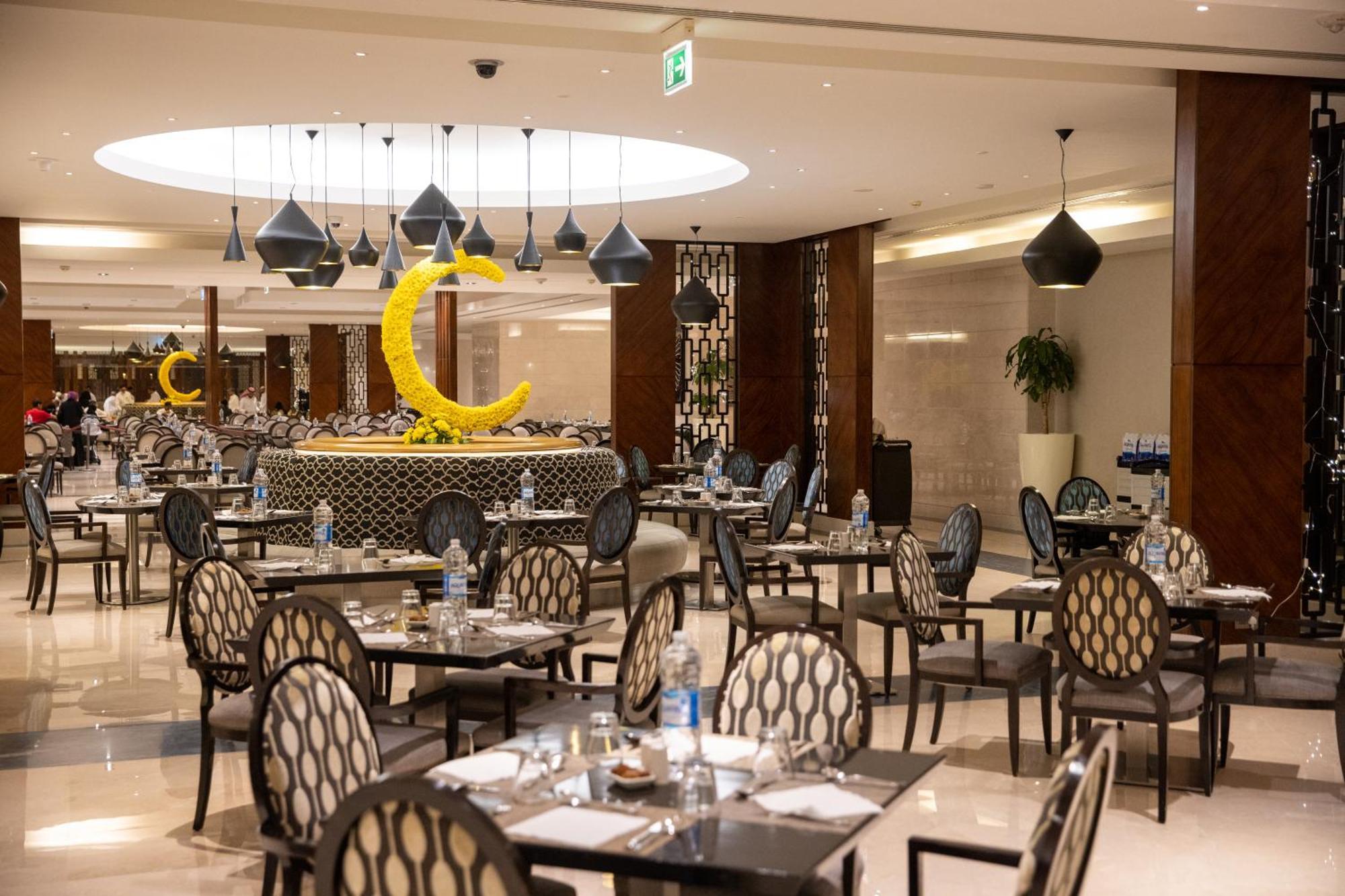 Swissotel Al Maqam Makkah Mekka Eksteriør billede The photo shows the interior of a restaurant that features a modern and elegant design. The space has several tables arranged with stylish chairs that have a circular pattern. There are pendant lights hanging from the ceiling in various shapes, provi