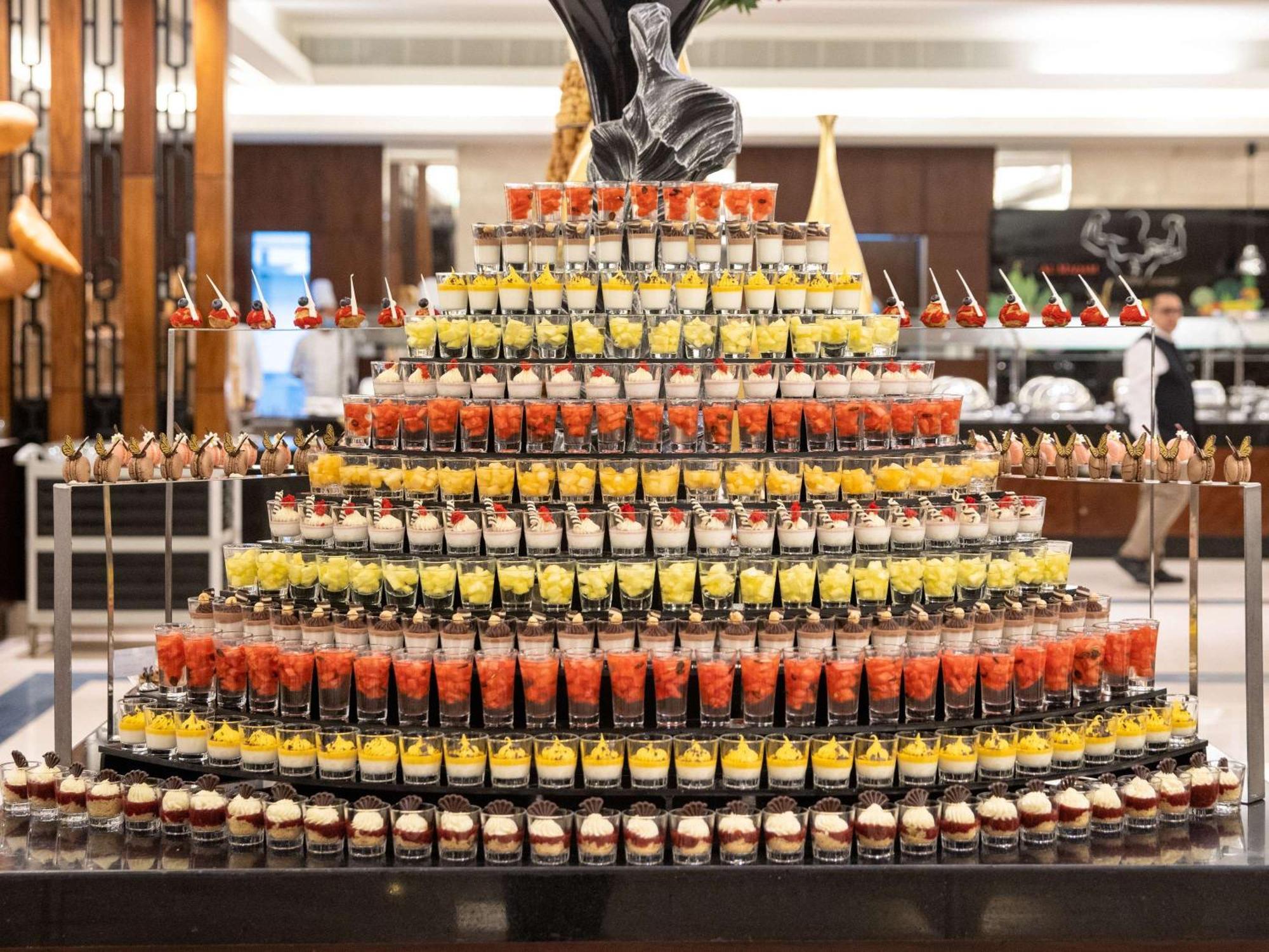 Swissotel Al Maqam Makkah Mekka Eksteriør billede The photo displays an impressive dessert display arranged in a pyramid shape. Each layer consists of numerous small dessert cups filled with different colorful treats. The top layer features a decorative element, possibly a statue or a centerpiece, w