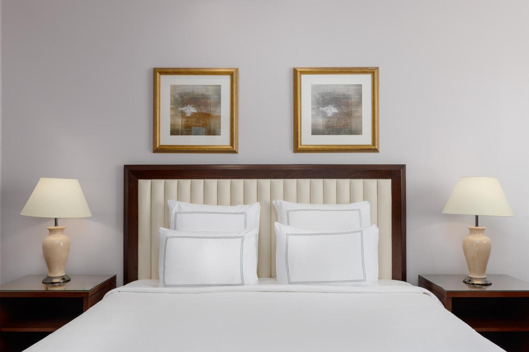 Swissotel Al Maqam Makkah Mekka Eksteriør billede The photo showcases a neatly arranged bedroom. It features a bed with a light-colored, tufted headboard and several white pillows neatly placed on it. On either side of the bed, there are wooden nightstands with lamps that have a soft, warm light. Ab